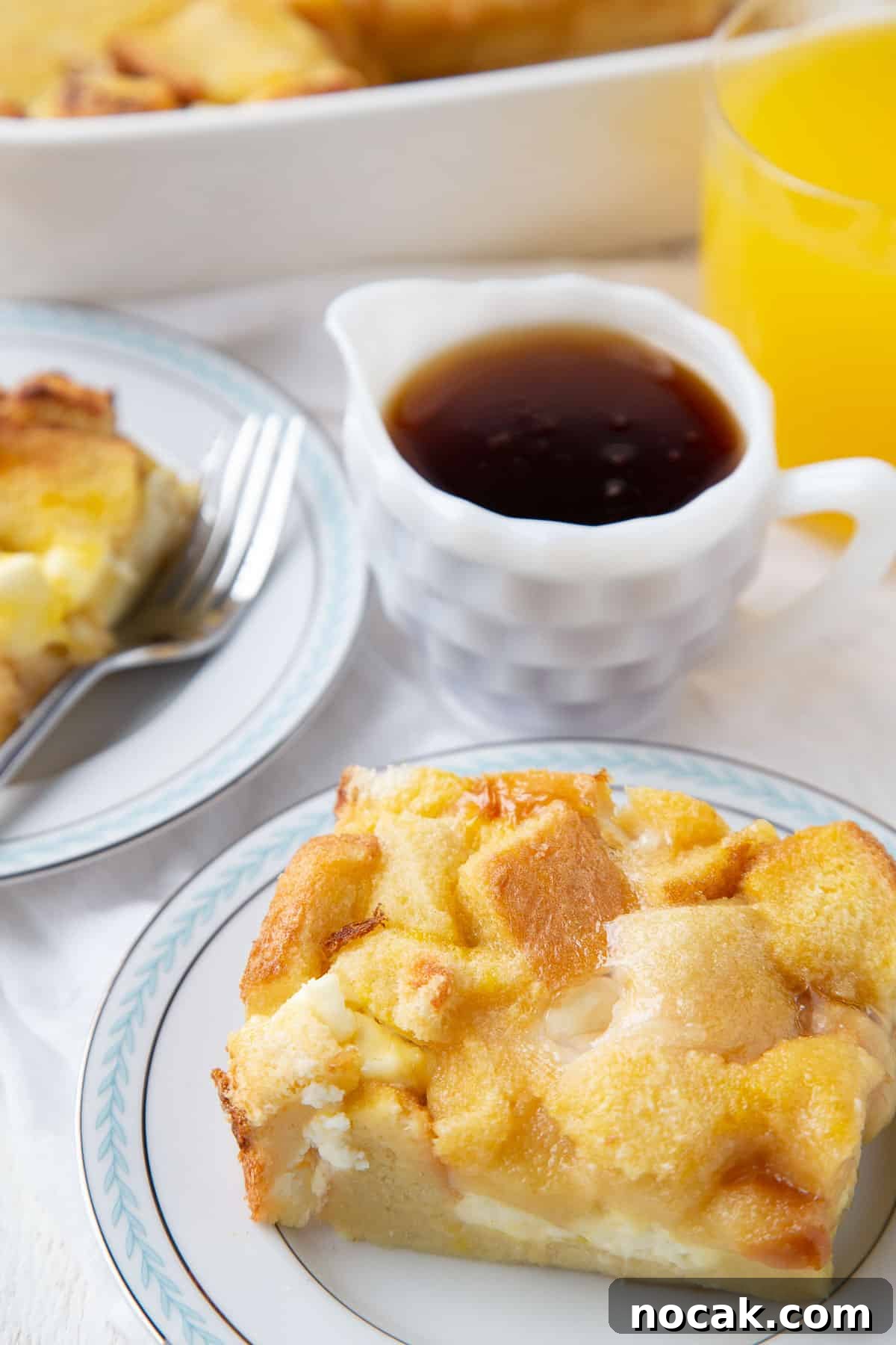 Baked Stuffed French Toast Casserole with Creamy Filling 2 slice of stuffed french toast casserole on a plate next to a mini pitcher of maple syrup.