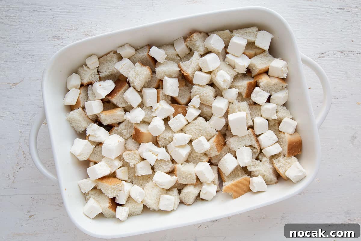 Baked Stuffed French Toast Casserole with Creamy Filling 5 bread cubes and cubes of cream cheese in a white casserole dish.