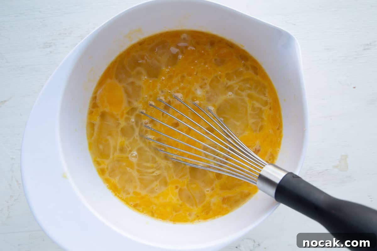 Baked Stuffed French Toast Casserole with Creamy Filling 6 beaten eggs and a whisk in a white mixing bowl.