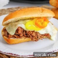Slow Cooker Italian Beef Sandwich Recipe for Tender, Flavorful Meat 7 Slow cooker Italian beef sandwich on a hoagie roll topped with provolone cheese and banana peppers on a white plate.