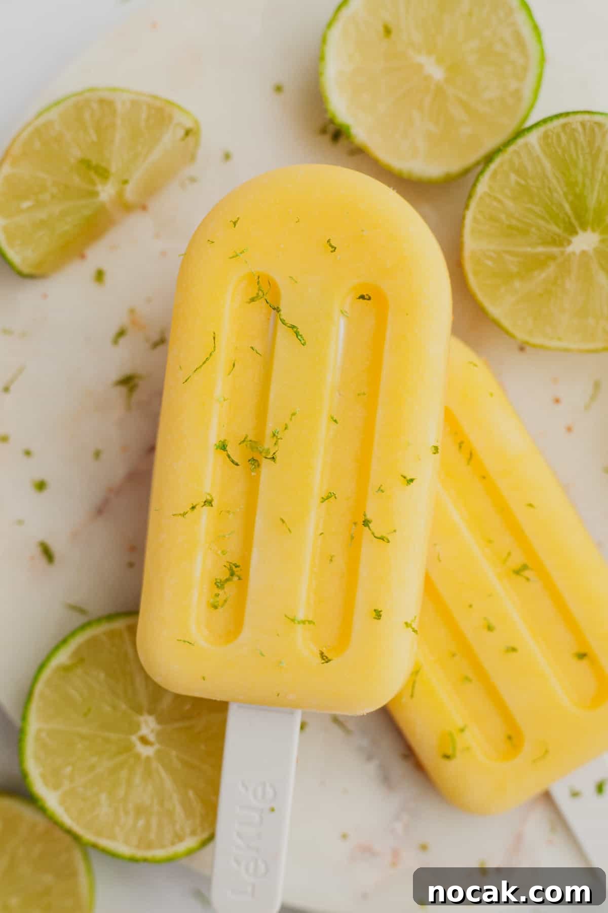 Two mango popsicles on a white plate with some slices of lime.