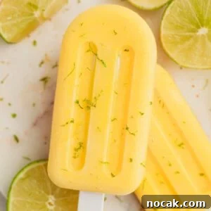 Two mango popsicles on a white plate with some slices of lime.