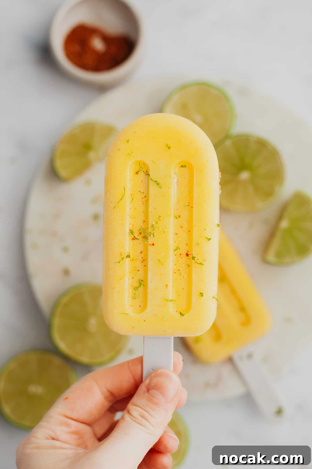 Two mango popsicles on a white plate with some slices of lime.