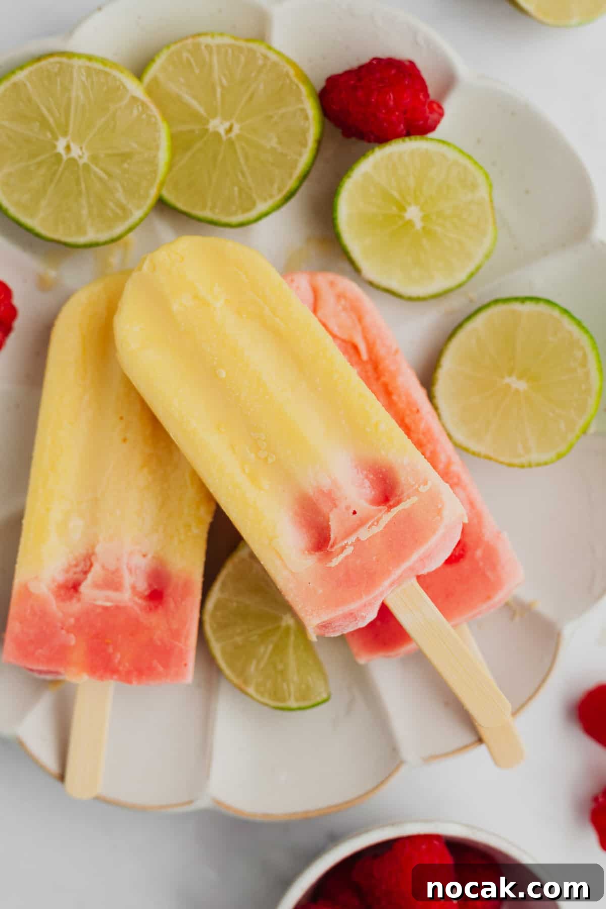 Three popsicles that are mango and raspberry flavored.