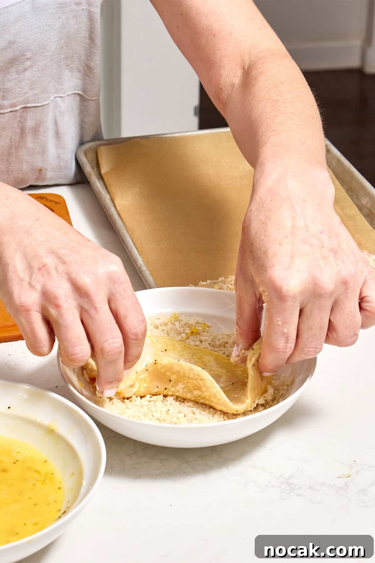 Crispy Breaded Chicken Cutlets: Step-by-Step Coating Guide 2 Woman dredging egg-coated chicken cutlet in panko breadcrumbs.