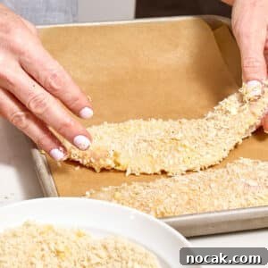 Crispy Breaded Chicken Cutlets: Step-by-Step Coating Guide 13 Woman placing breaded chicken cutlet on parchment-lined baking sheet.