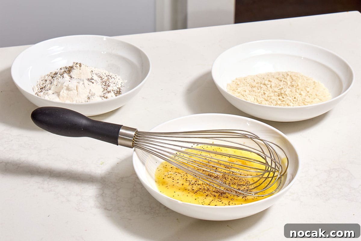 Crispy Breaded Chicken Cutlets: Step-by-Step Coating Guide 4 Seasoned flour, beaten eggs, and breadcrumbs in shallow white bowls on counter.