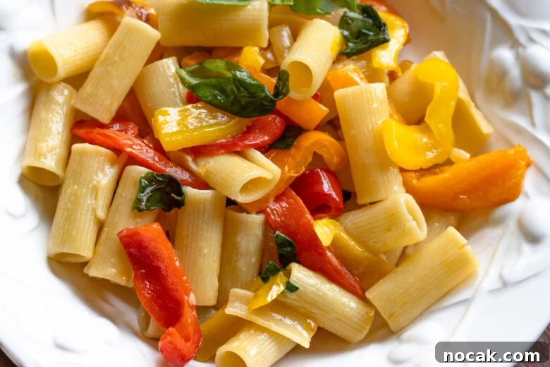 Close up of the roasted bell pepper sauce with the pasta in a white large rimmed pasta dish.