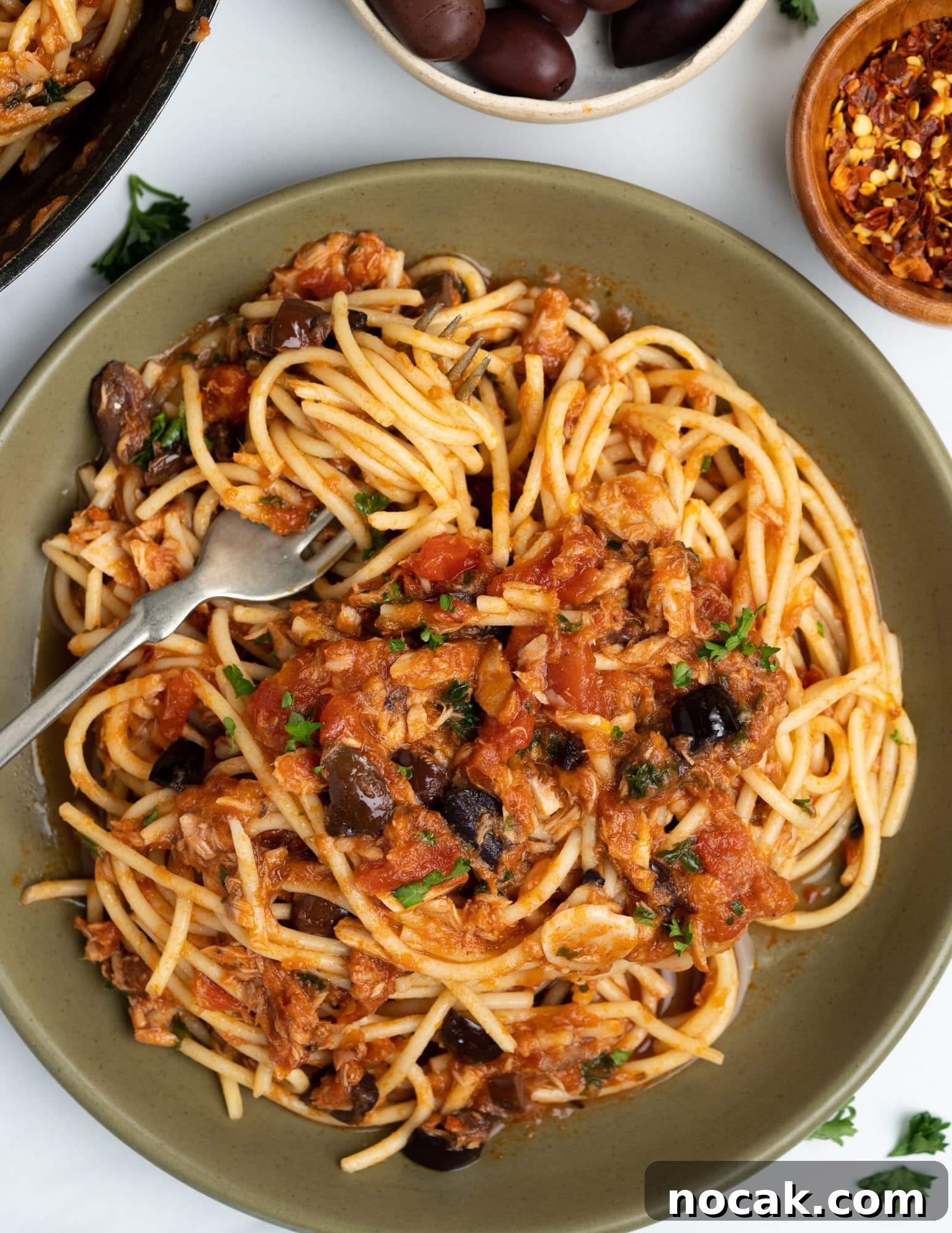 Tomato tuna pasta with Spaghetti, tomato and tuna sauce with olives and seasonings, garnished with parsley.
