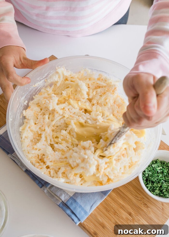 Cracker Barrel Hashbrown Casserole Copycat Recipe 14 A person stirring shredded potatoes in a bowl during preparation of a hashbrown casserole.