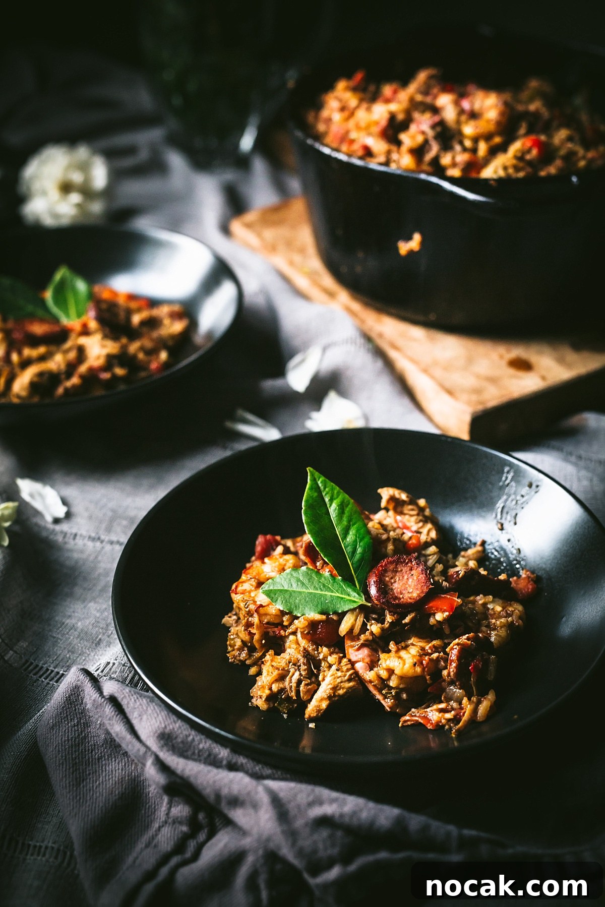 Paul Prudhomme’s Dutch Oven Jambalaya Recipe 10 backlit shot of Cajun Jambalaya in black bowl garnished with bay leaf