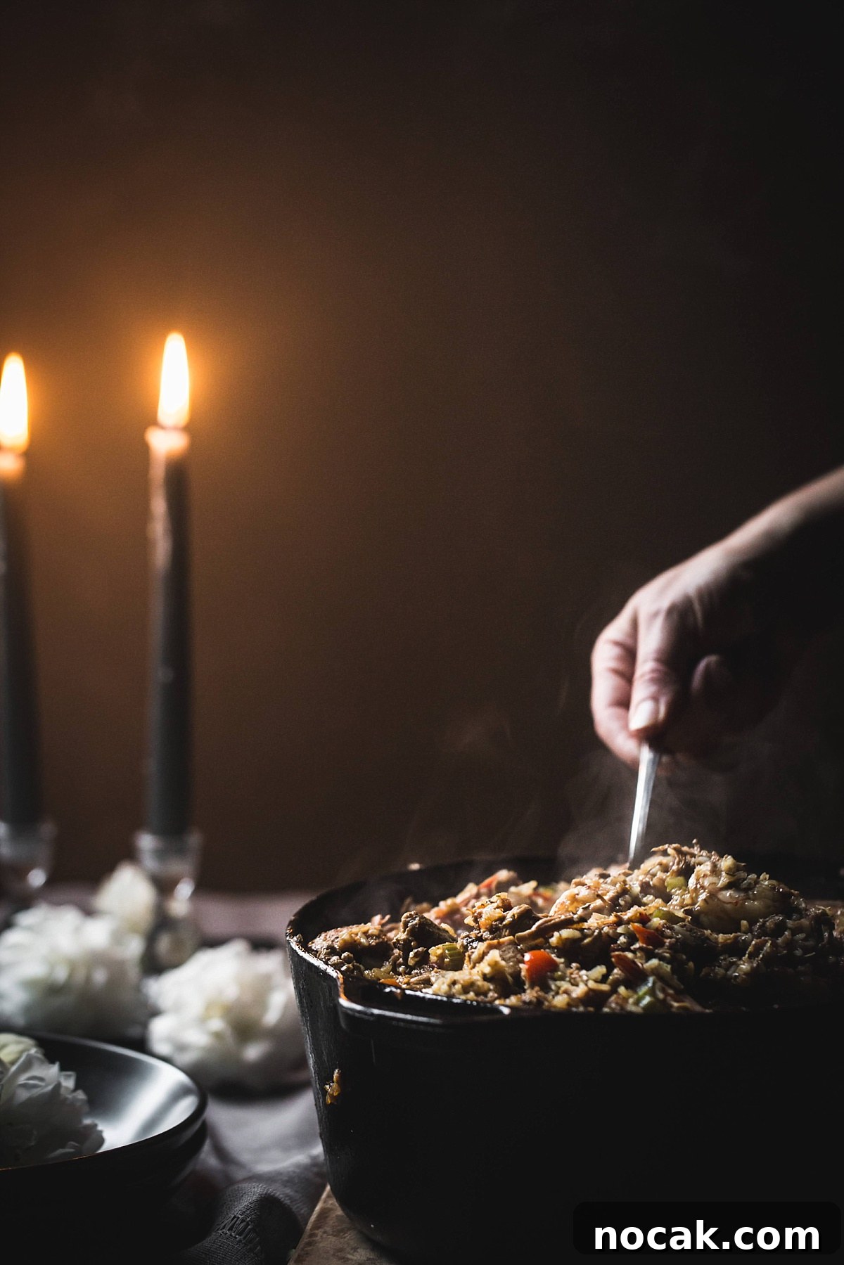 Paul Prudhomme’s Dutch Oven Jambalaya Recipe 3 closeup shot of hand scooping out Jumbalaya in candlelight