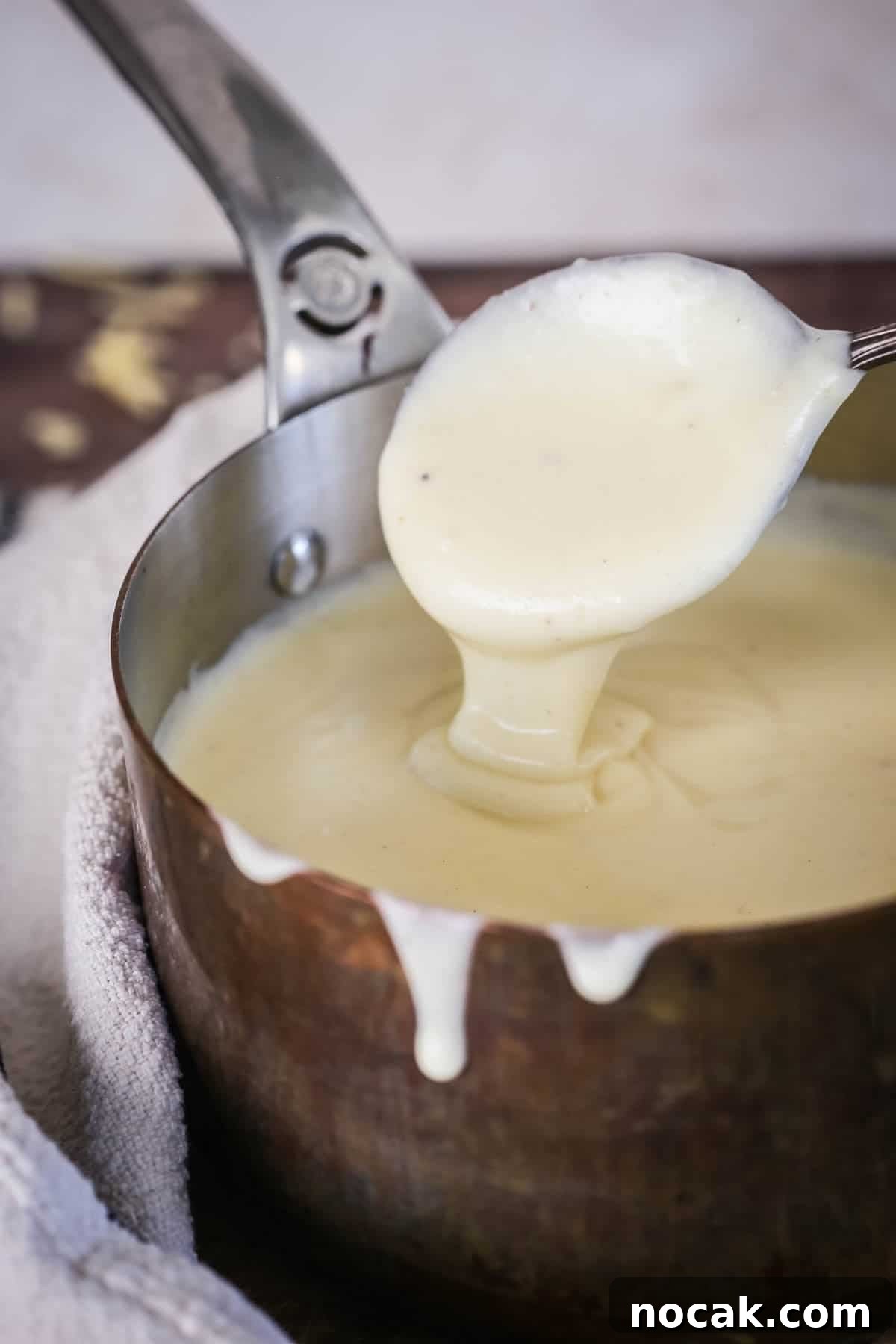 Creamy Gluten-Free Cheese Sauce Recipe for Dips & Pasta 2 Spooning gluten-free cheese sauce from saucepan showing velvety creamy texture.