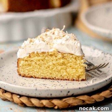 A slice of coconut almond cake on a plate with a fork next to it.