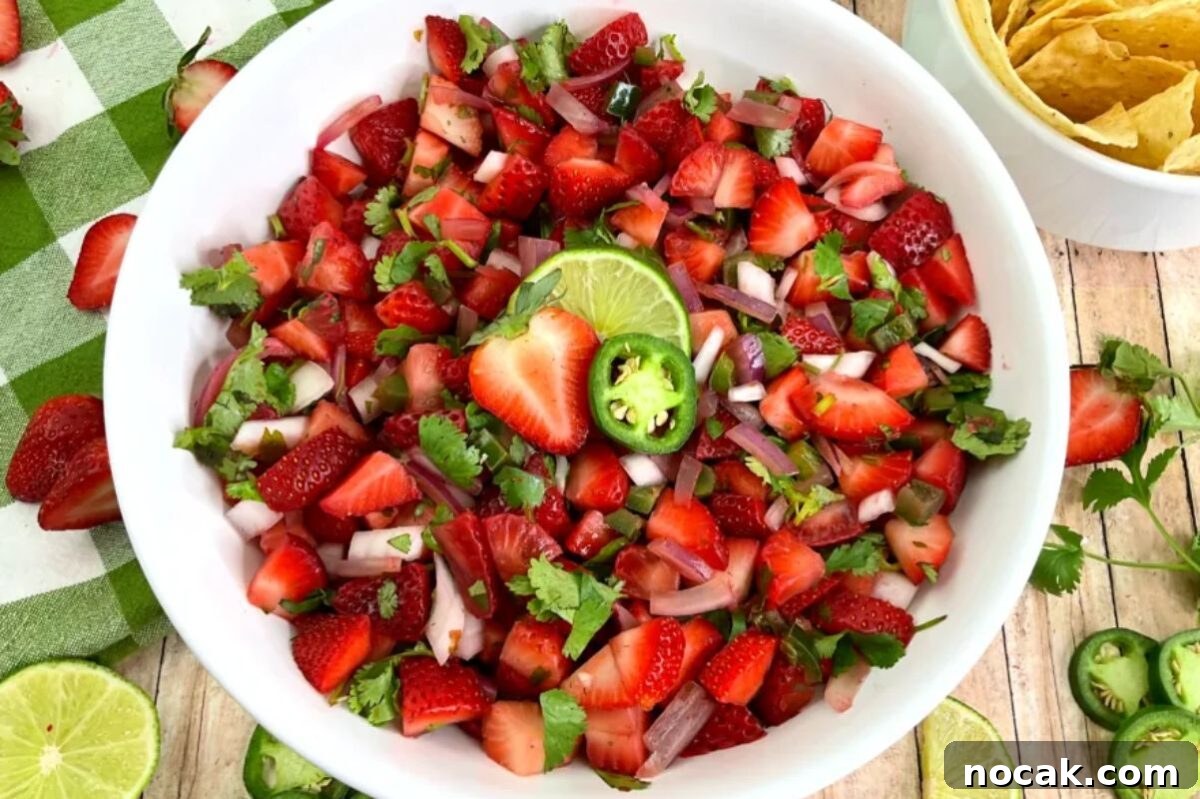 35 Easter Appetizers to Kick Off Your Holiday Feast 15 A bowl of strawberry salsa garnished with lime and jalapeño on a table with a napkin and tortilla chips on the side, serving as a festive Easter appetizer.