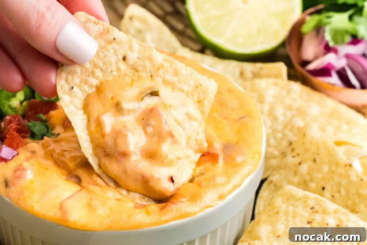 35 Easter Appetizers to Kick Off Your Holiday Feast 35 A hand dipping a tortilla chip into a bowl of creamy cheese dip with lime and cilantro in the background, perfect for an Easter appetizer.