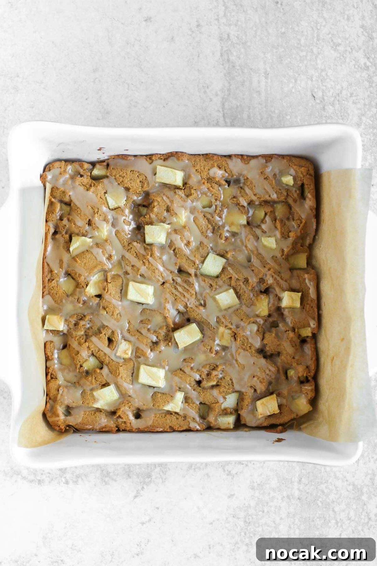Uncut apple blondie bars with glaze in a square baking dish.