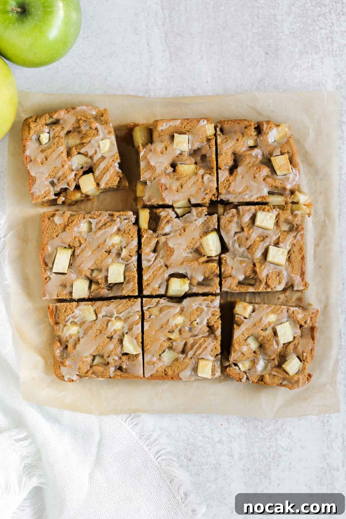 Cut up apple blondie squares with glaze on parchment paper.