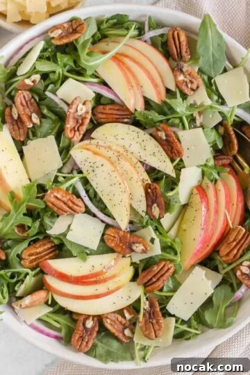 Arugula and apple salad with pecans, parmesan cheese, and red onion in a large salad bowl with vintage silverware.