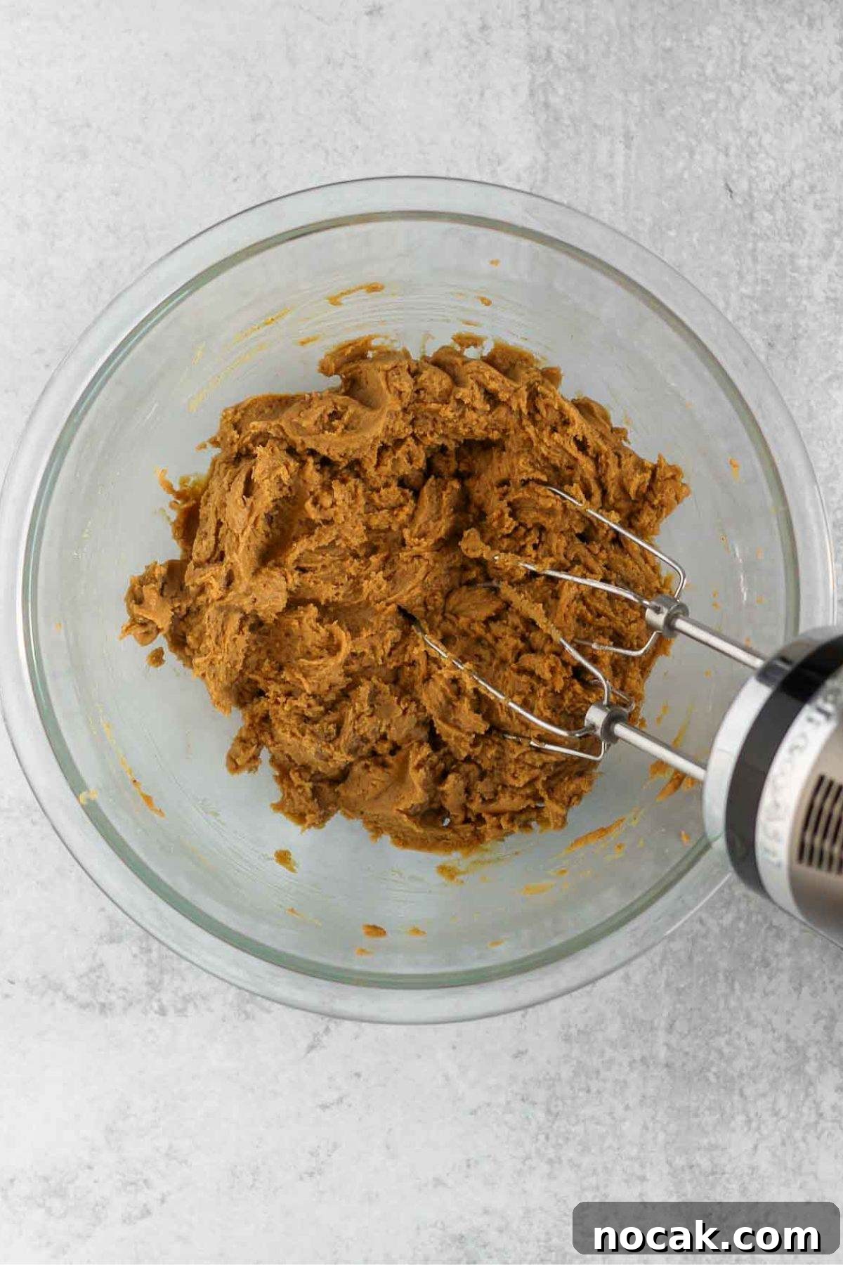 Apple blondie dough/mix being mixed with a hand-mixer in a glass mixing bowl.