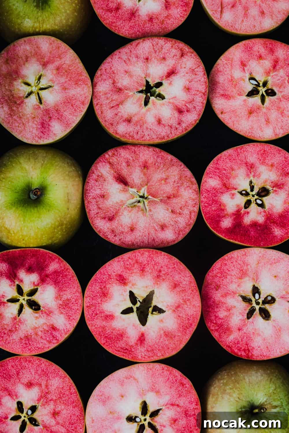 pink hidden rose apples, cut in half, overhead shot on a black background.