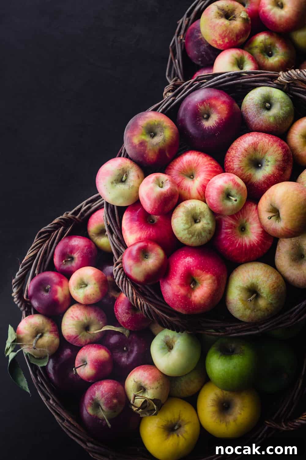 3 different baked filled with fresh apples in all colors of the rainbow; overhead on a black background.