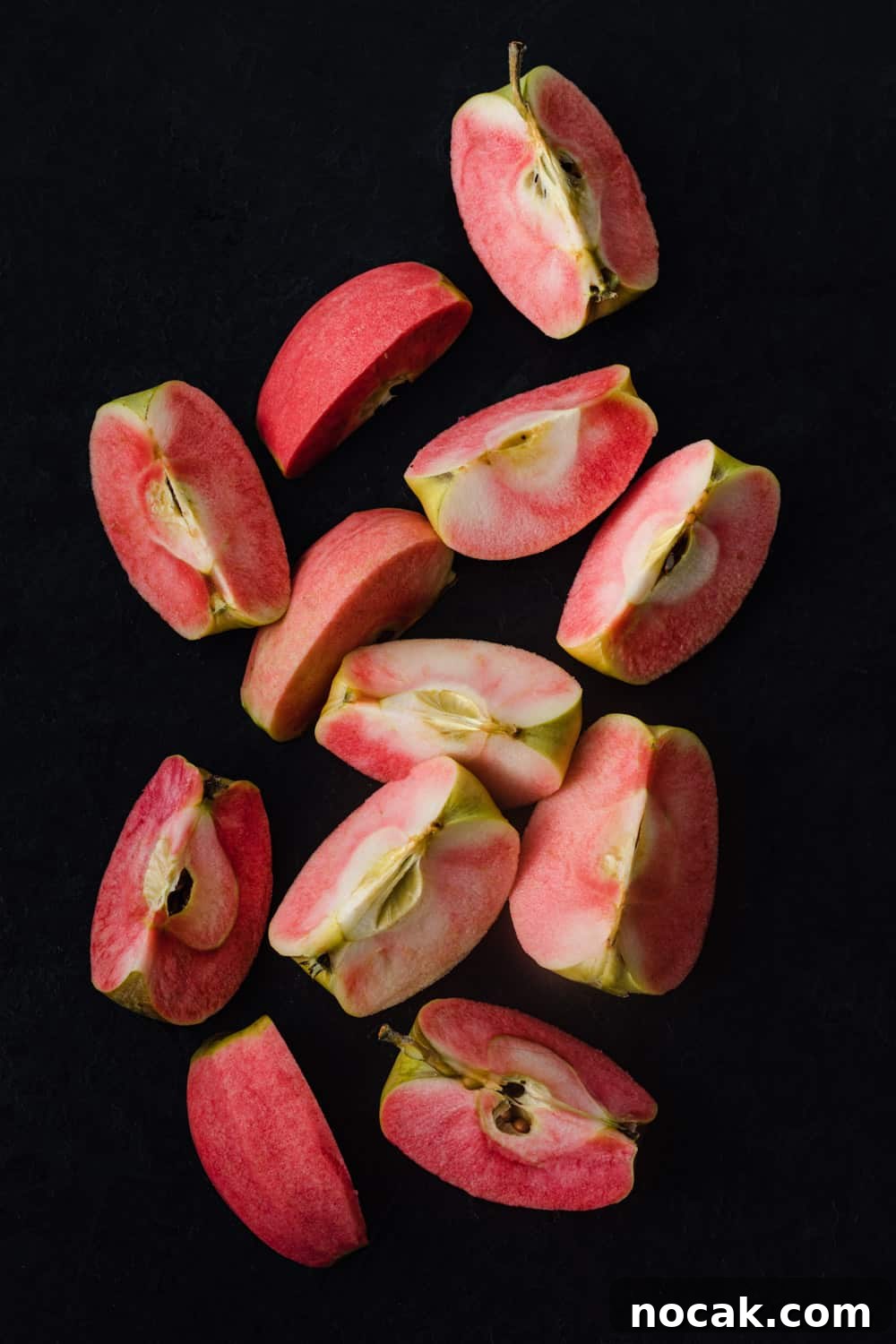 pink hidden rose apples, cut into wedges, overhead shot on a black background.