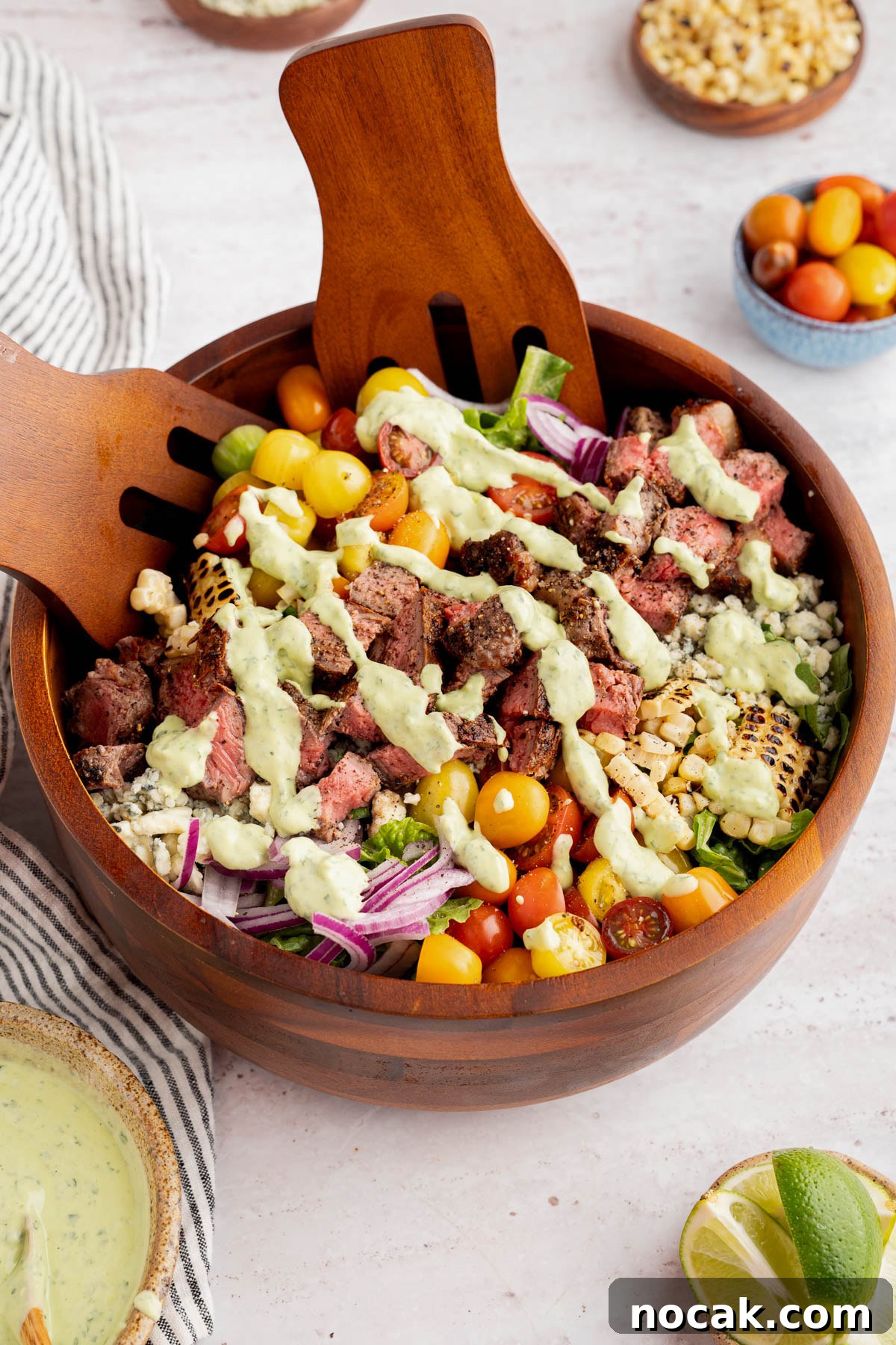 Steak Salad with Avocado-Lime Cilantro Crema Recipe 12 The steak salad with the avocado-lime cilantro crema drizzled on top in a bowl on a countertop. Two serving forks sit inside the bowl.