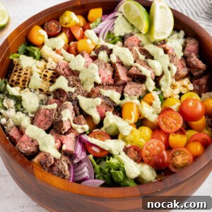 Steak Salad with Avocado-Lime Cilantro Crema Recipe 13 The steak salad with cilantro-lime avocado crema drizzled on top in a wooden bowl on a white countertop.