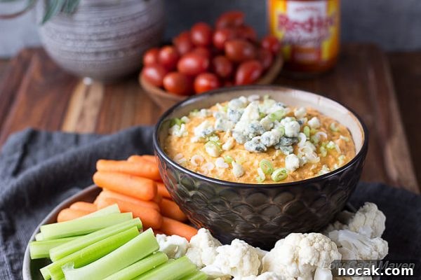 Keto Buffalo Chicken Dip Recipe — Low Carb, Creamy & Spicy 3 Buffalo Chicken dip topped with scallions and blue cheese in a bowl with raw vegetables.