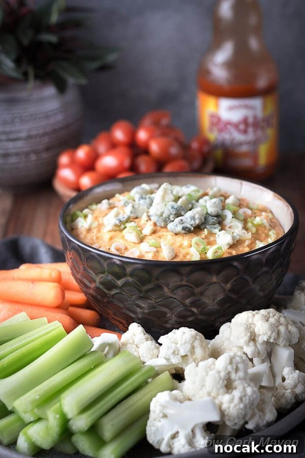 Keto Buffalo Chicken Dip Recipe — Low Carb, Creamy & Spicy 4 Buffalo Chicken dip topped with scallions and blue cheese in a bowl with raw vegetables and Frank's Red Hot Buffalo Sauce.