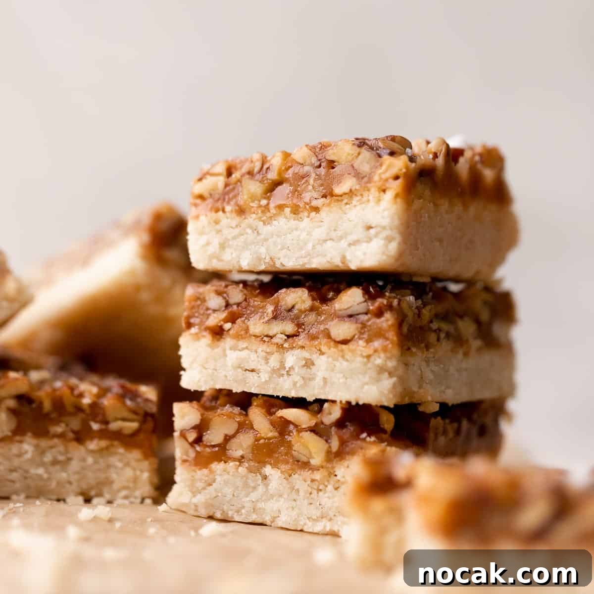 Salted Caramel Pecan Bars Recipe — Chewy Pecan Caramel Squares 11 caramel pecan bars in a stack on parchment paper.