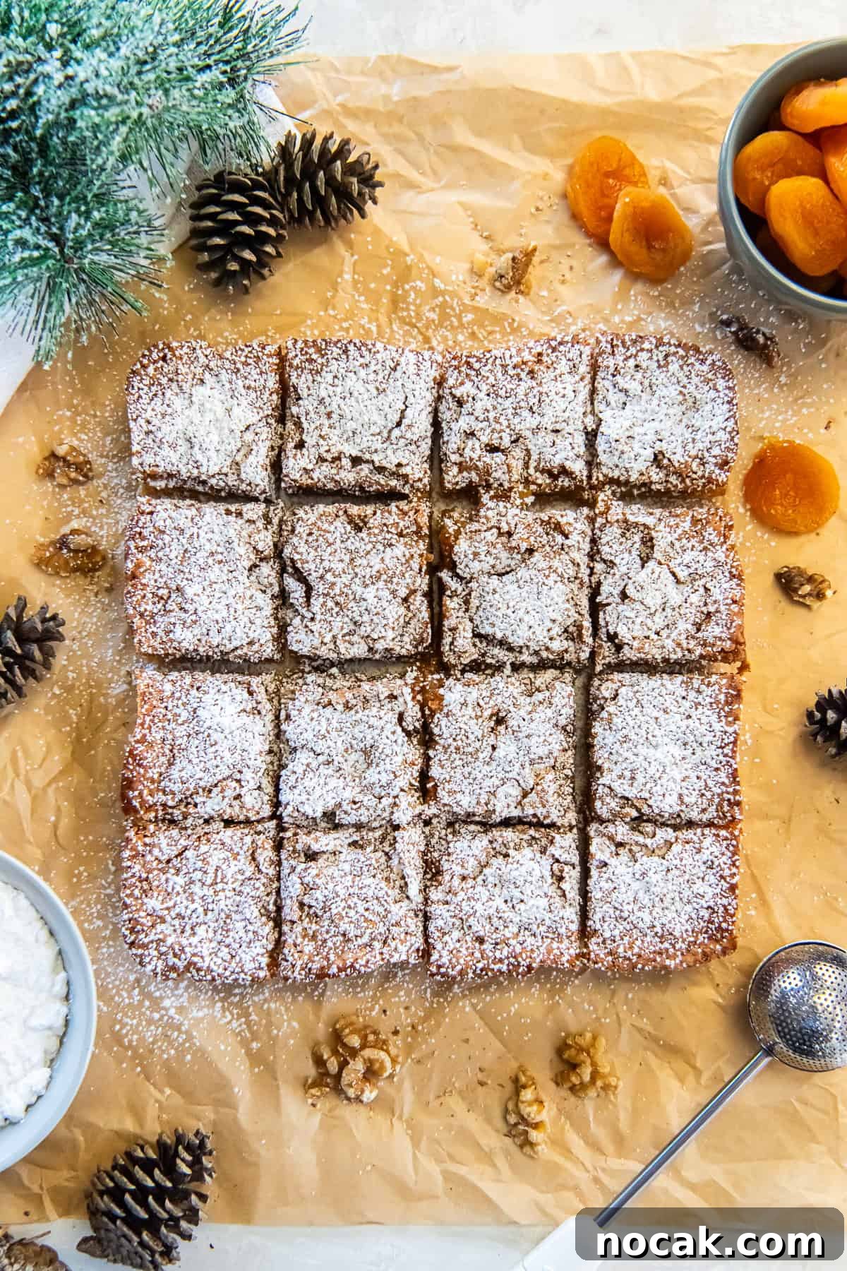 Chewy Apricot Bars with Oat Crust and Almond Glaze 3 Apricot bars dusted with powdered sugar, cut into squares on parchment paper.