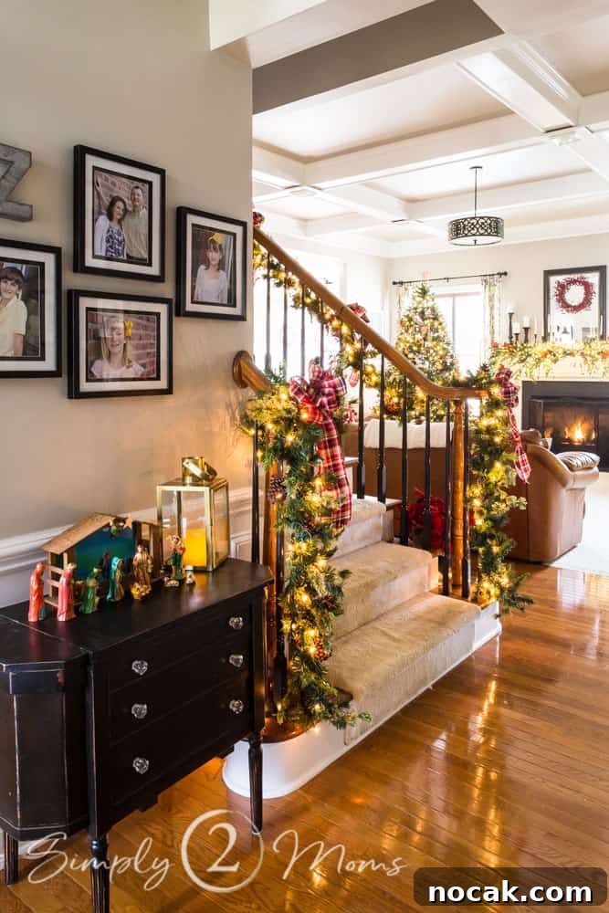 view of front entry with nativity scene, staircase, andfamily room decorated for Christmas with twinkle lights on the Christmas tree, fireplace mantle, garland on the staircase, and red berry wreath on mirror over fireplace mantel