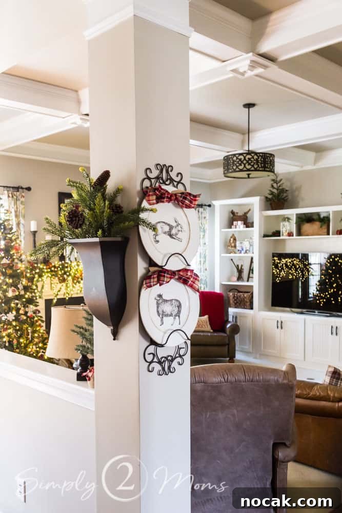 plates on decorative plate rack with red plaid bows, sconce filled with greenery both hanging on column leading to a family room decorated for Christmas in the background