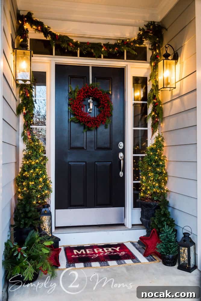 black front door with sidelights decorated for Christmas with topiaries in urns, boxwood garland, red berry wreath, layered wreath, lanterns, layered welcome mat, fresh greenery arrangement
