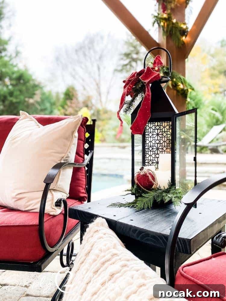 Black metal candle lantern with greenery in the bottom and candles and a red Christmas ball on top. Large red bow with more greenery is tied on the handle.