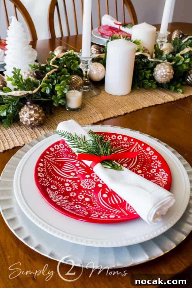 view of table set for Christmas with red and white plates, burlap runner, boxwood garland, white candles and mercury glass ornaments