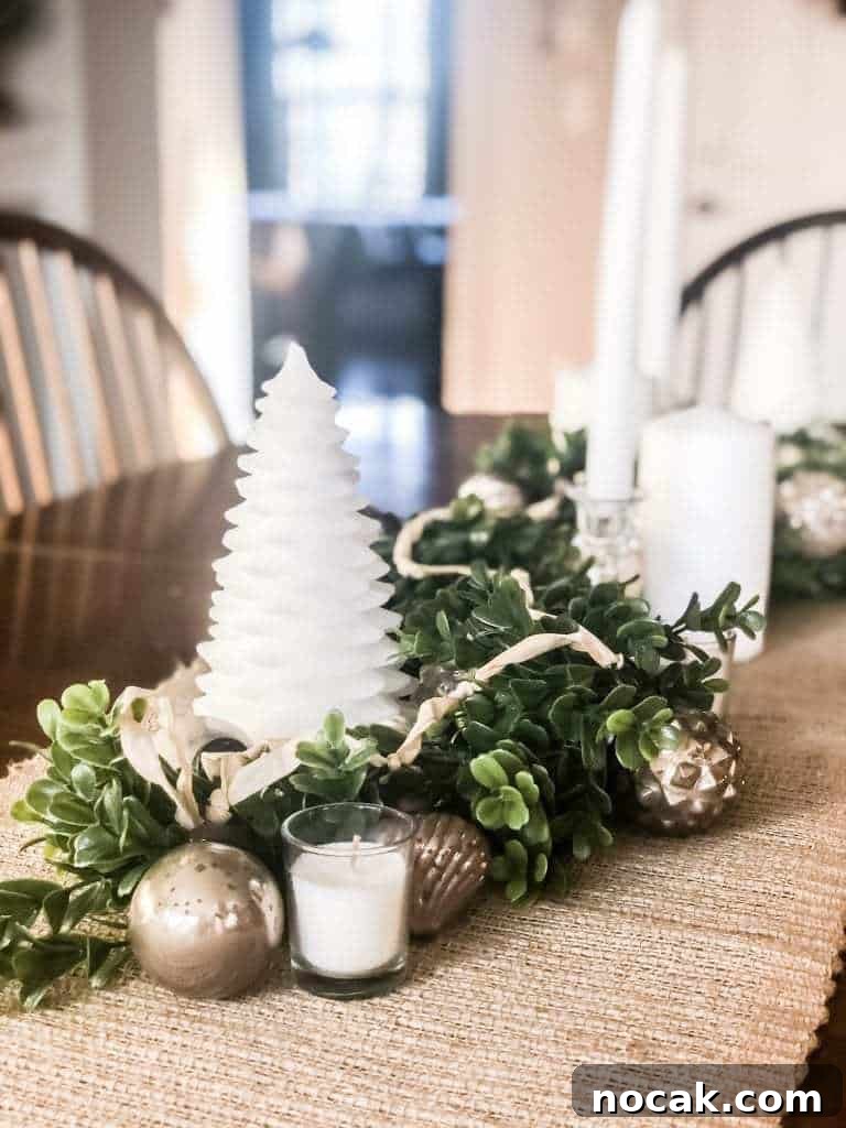 view of Christmas centerpiece of boxwood garland, white candles, and vintage mercury glass ornaments on burlap table runner