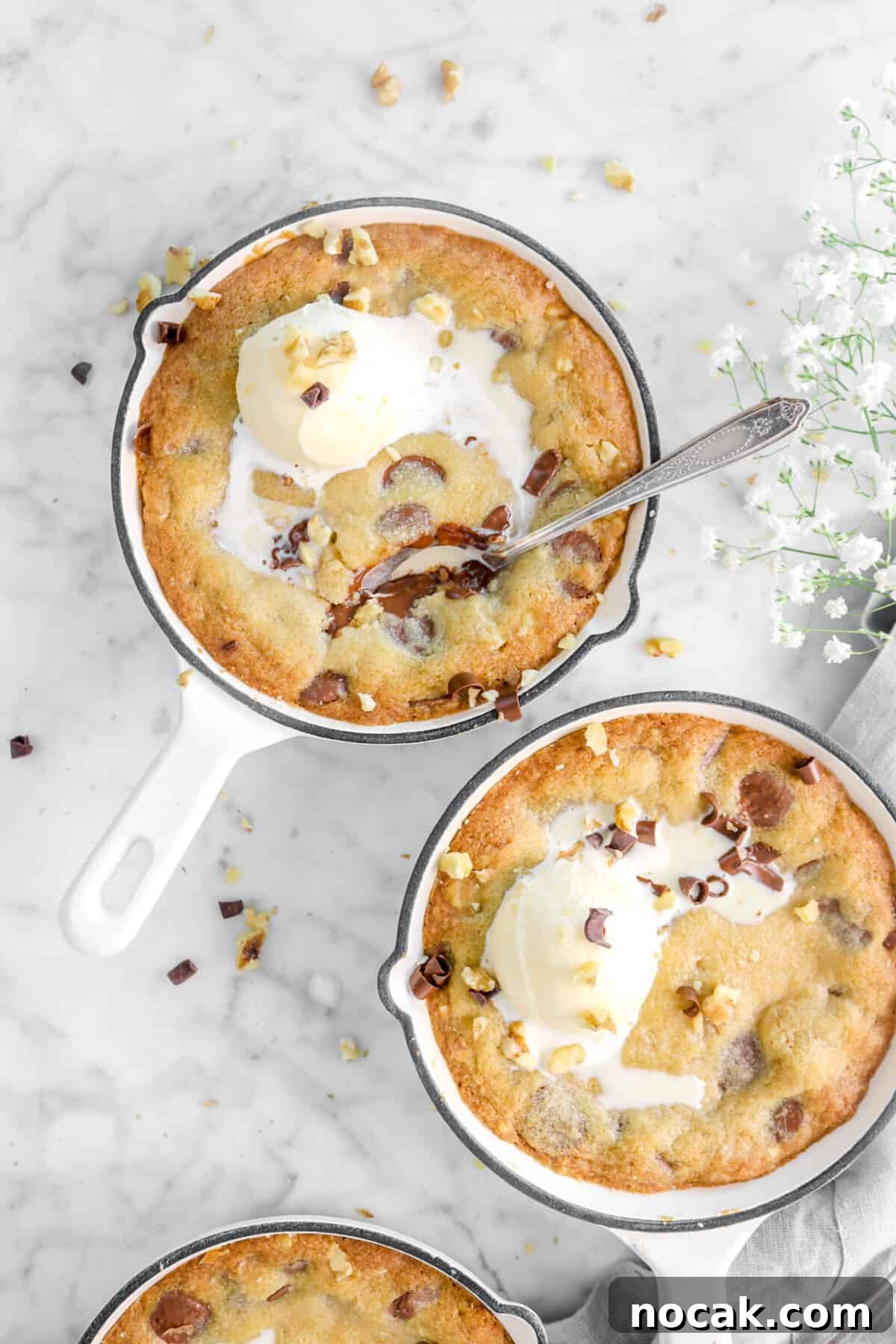 two skillet cookies with a spoon in one with ice cream and white flowers