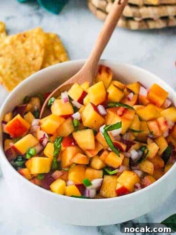 Small wooden spoon in a bowl of peach salsa.