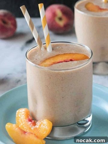 Two peach slices next to an almond butter smoothie on a blue plate.