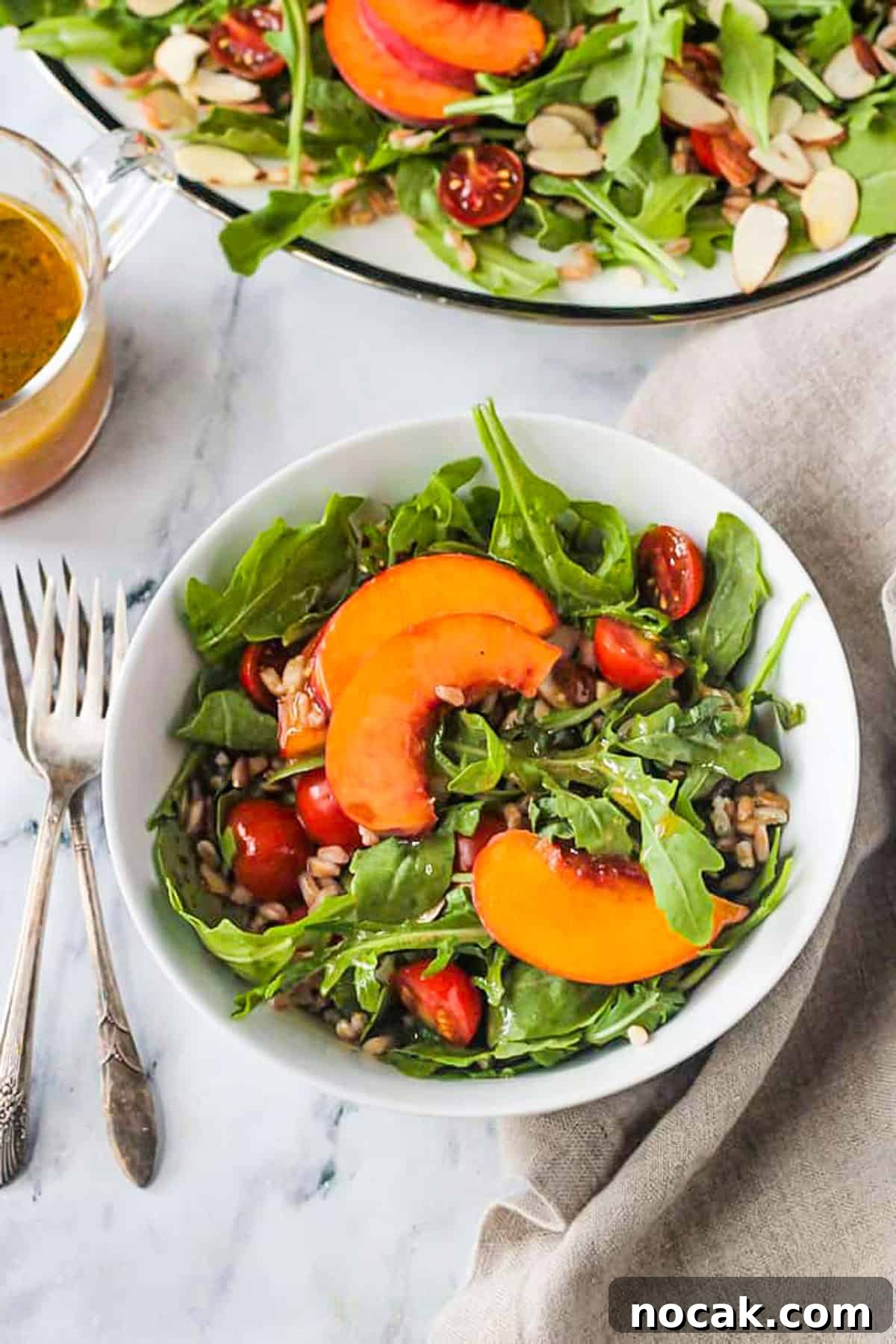 Arugula, Peach & Farro Salad with Orange Vinaigrette 10 Bowl of arugula peach salad next to two forks.