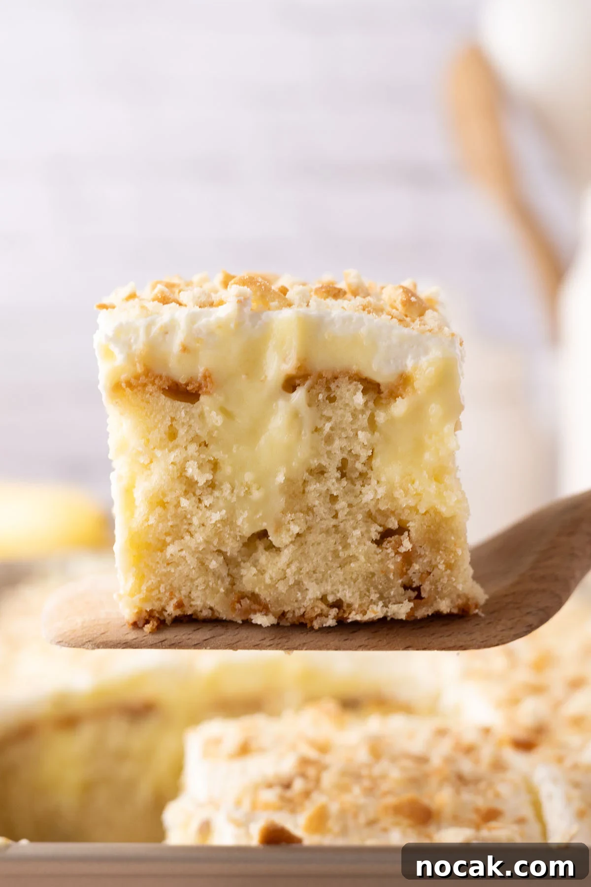 Creamy Banana Pudding Poke Cake Recipe for Dessert Fans 12 Slice of Banana Pudding Cake on a wooden serving spoon.