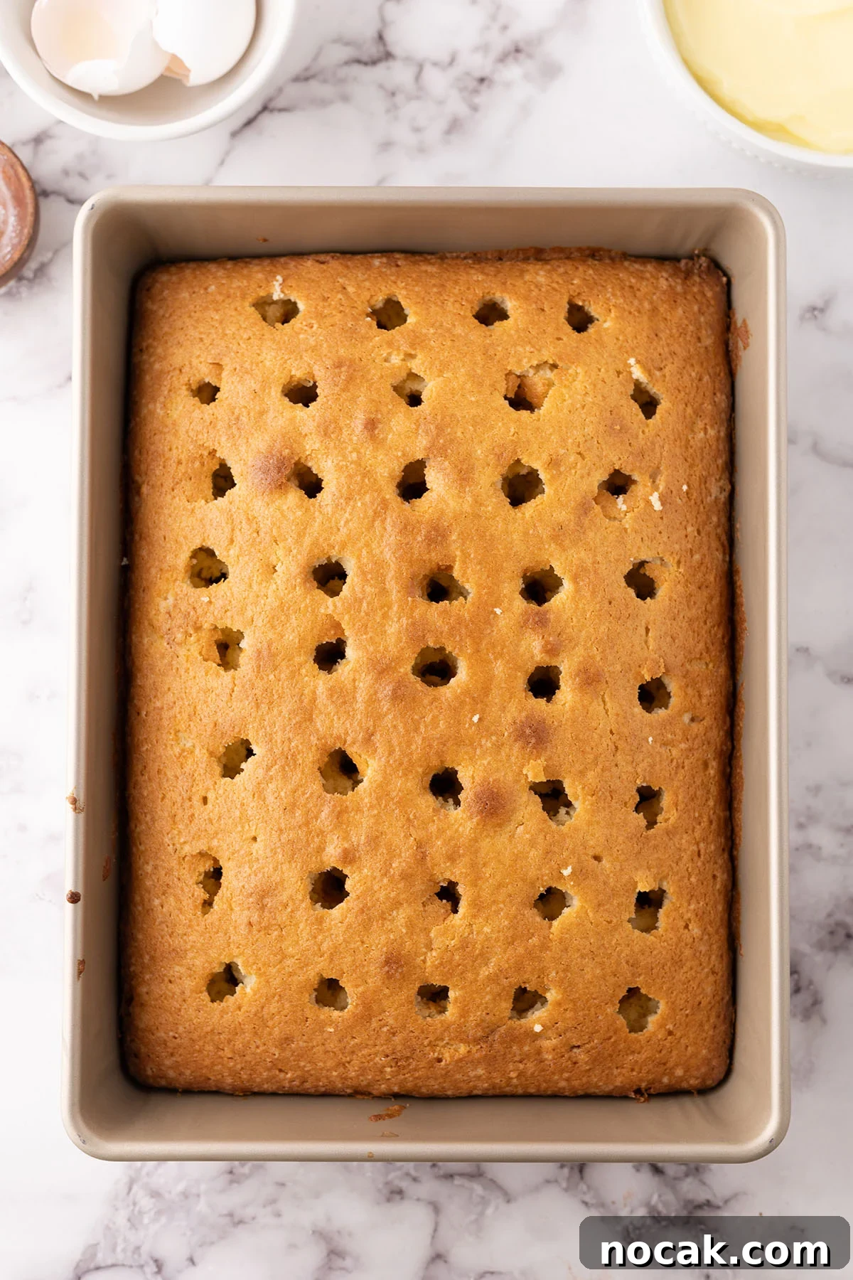 Creamy Banana Pudding Poke Cake Recipe for Dessert Fans 8 Baked cake with holes poked in the top.