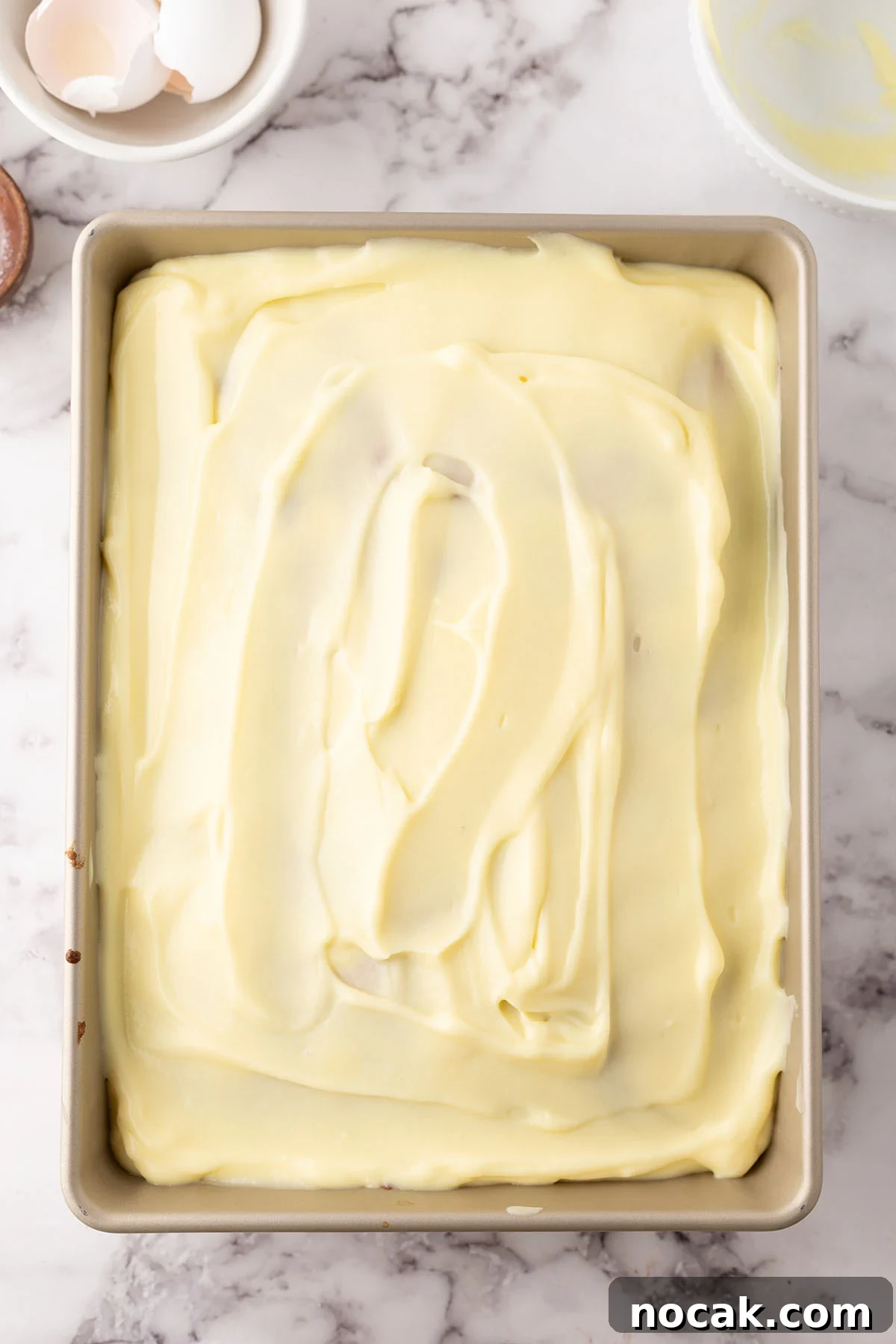 Creamy Banana Pudding Poke Cake Recipe for Dessert Fans 9 Banana pudding spread over top of cake in baking pan.