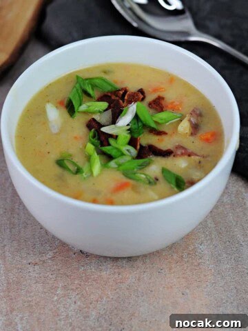 white bowl of cheesy potato soup garnished with bacon and green onion.