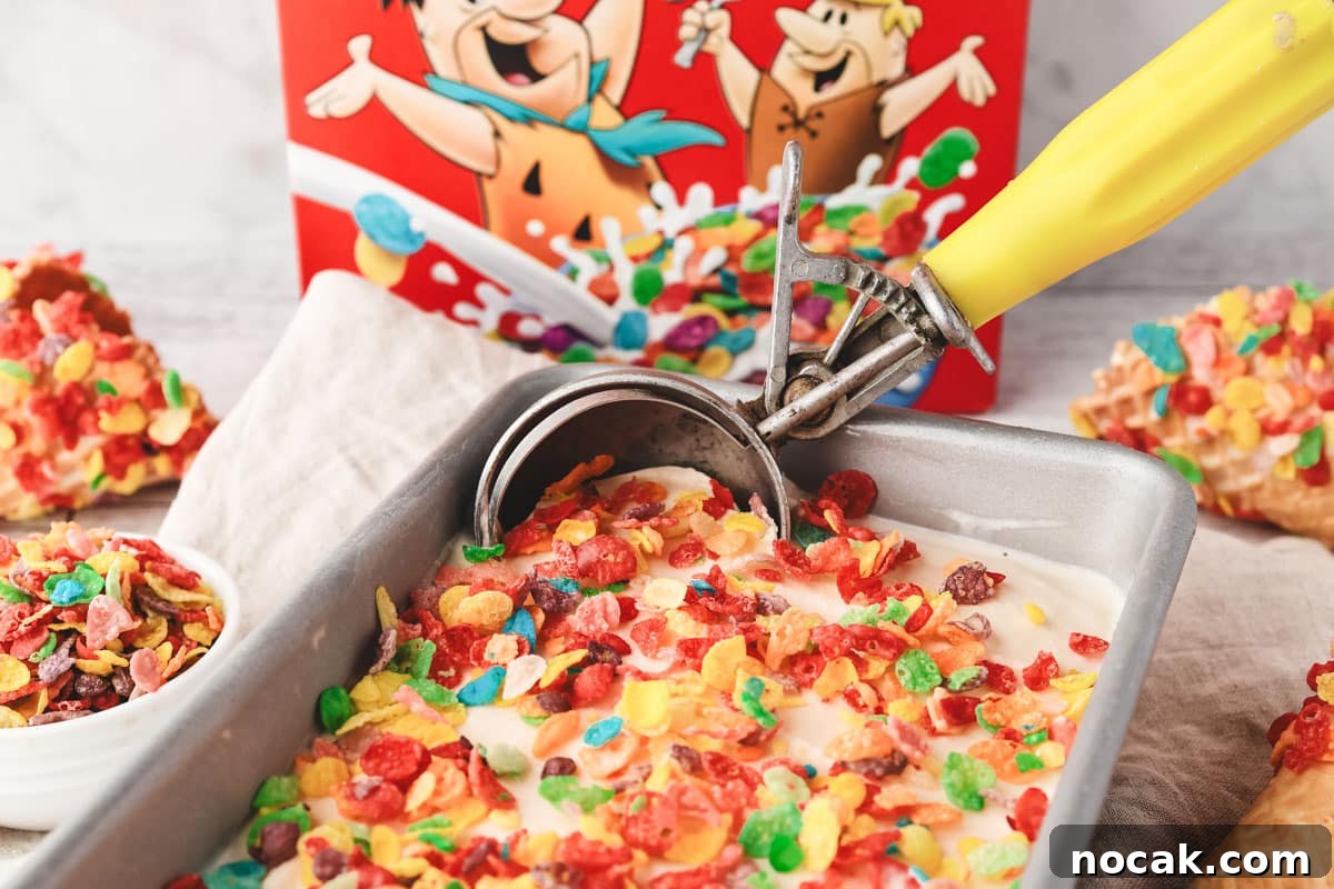 Fruity Pebbles Ice Cream Recipe: Nostalgic Cereal Ice Cream Treat 6 Scooping Fruity Pebbles ice cream from a pan, with box of Fruity Pebbles and Fruity Pebbles ice cream cones in the background.