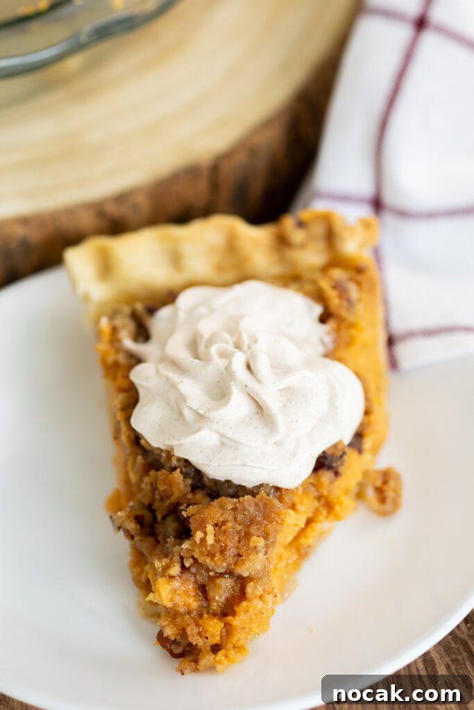Southern Sweet Potato Pie with Crunchy Crumble Topping 2 A front view of a piece of southern sweet potato pie on a white plate topped with a swirl of whipped cream.