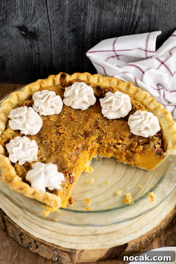 Southern Sweet Potato Pie with Crunchy Crumble Topping 3 A southern sweet potato pie in a glass pie dish topped with swirls of whipped cream, all on a rustic wood background with a linen napkin behind.